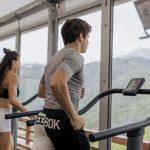 Two people running on treadmills in a gym with a mountain view, promoting fitness.